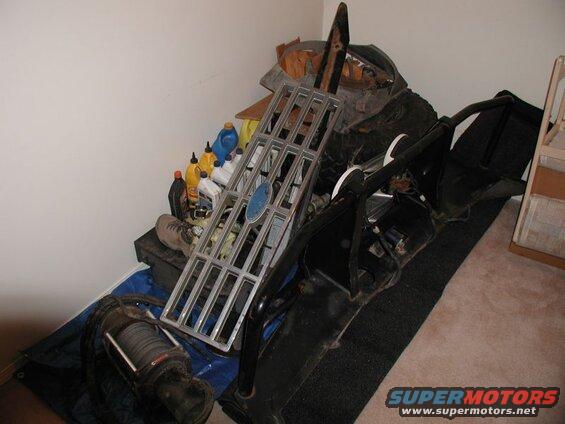 Vehicle parts including a chrome grille, winch, and roll cage stored in a room.