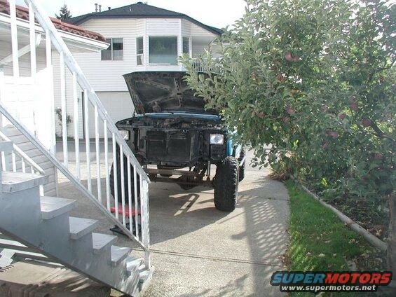 1985 Ford Bronco with hood open, parked on driveway next to apple tree and outdoor stairs.