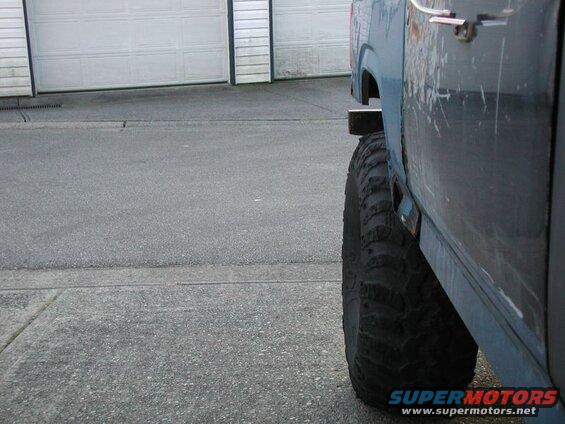 Side view of a blue vehicle's rear fender and large off-road tire.
