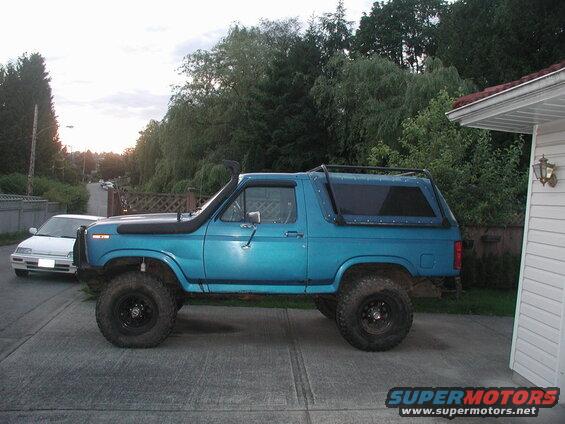 Teal lifted Ford Bronco with snorkel and roof rack parked on driveway.