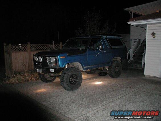 Blue lifted Ford Bronco with brush guard and off-road tires parked at night.