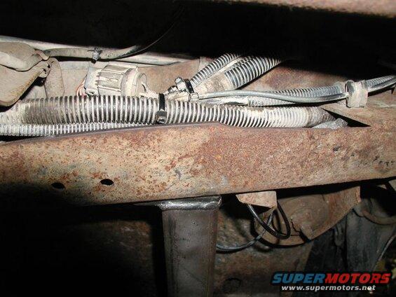 Underside of a vehicle showing rusty frame, wires, and a metal support.