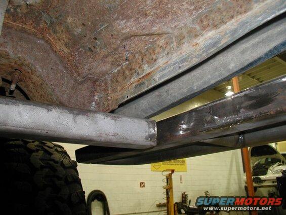 Underside of a vehicle with rusted frame and new metal reinforcements.