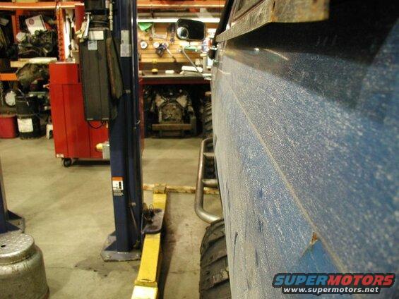 Dusty blue vehicle side panel with tire and running board visible, in a garage setting.