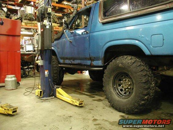 Blue 1985 Ford Bronco on a lift in a garage, showing off-road tires and snorkel.