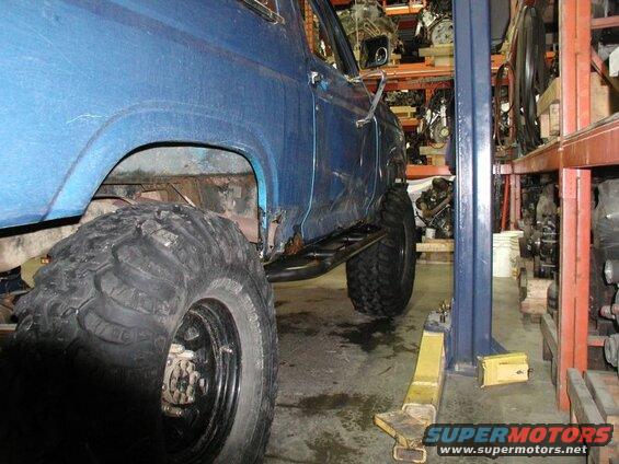 Blue Ford Bronco on a lift with large tires, showing rust on the body.