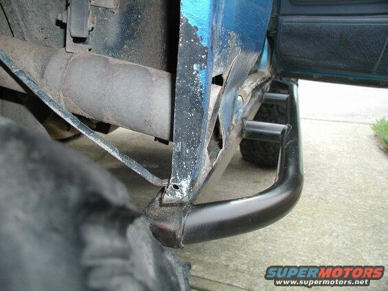 Close-up of rusted rocker panel and black rock sliders on a blue vehicle.