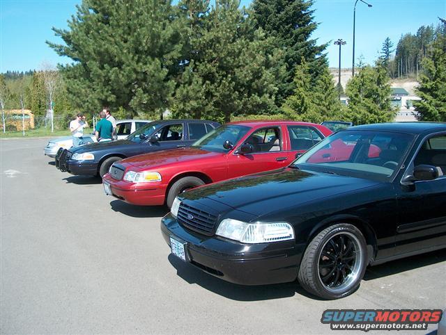 Several Ford Crown Victorias parked in a lot. The closest one is black with custom wheels