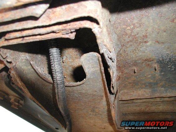 Underside of vehicle frame with heavy rust and a black conduit.
