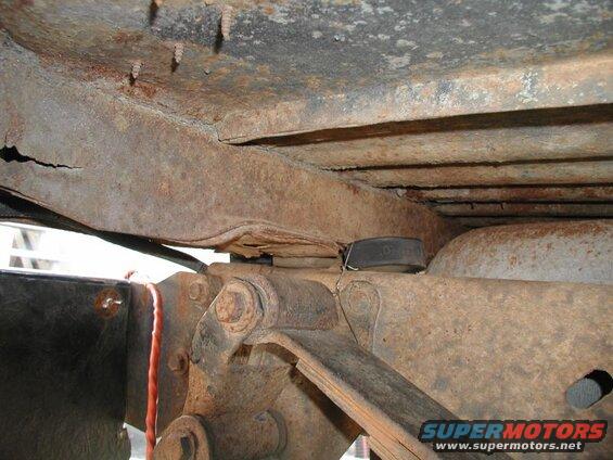 Heavily rusted underside of a vehicle frame with visible suspension parts.