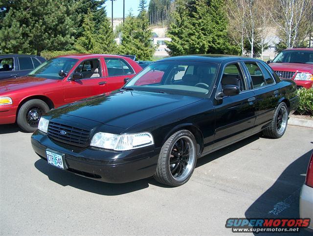 Black 2001 Ford Crown Victoria with aftermarket wheels, parked next to a red Ford Crown Victoria
