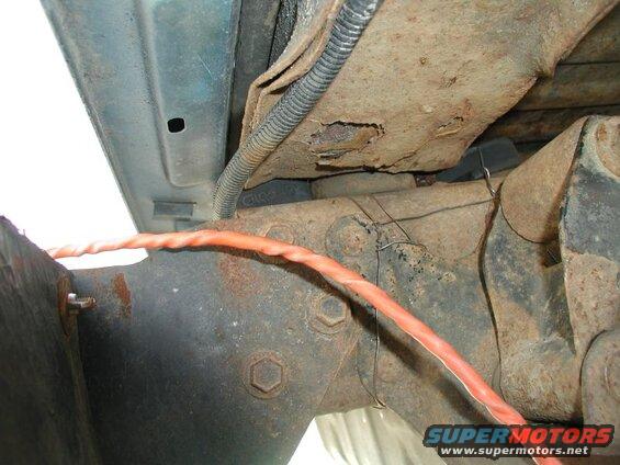 Close-up of rusty vehicle undercarriage with orange wire.