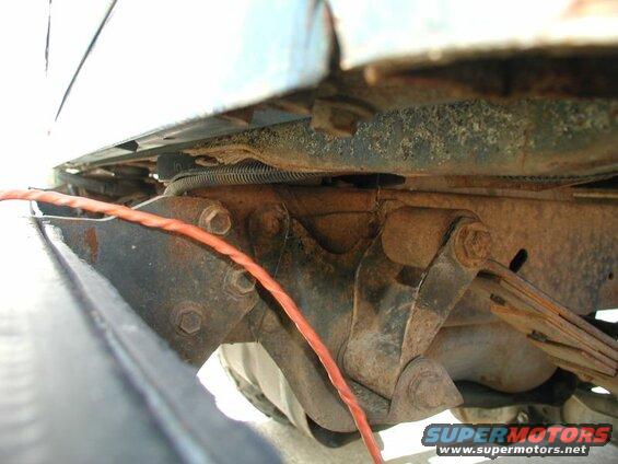 Underside of vehicle frame with rusty leaf spring suspension and orange wire.