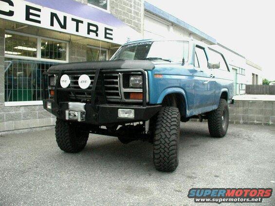 Blue 1985 Ford Bronco with brush guard and off-road tires parked outside.