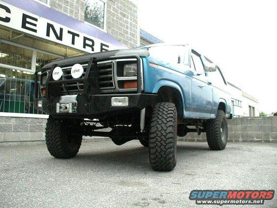 Lifted blue 1980s Ford Bronco with brush guard and off-road tires parked outside.