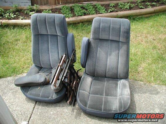 Two dark gray velour car seats with armrests on a concrete patio.
