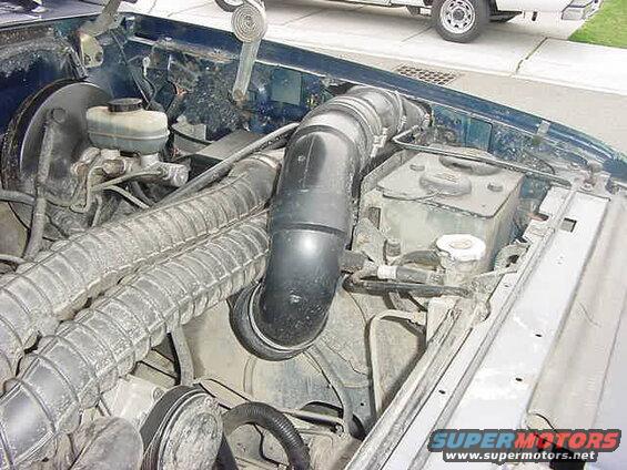 Engine bay of a dark blue Ford Bronco, showing air intake hoses and brake fluid reservoir.