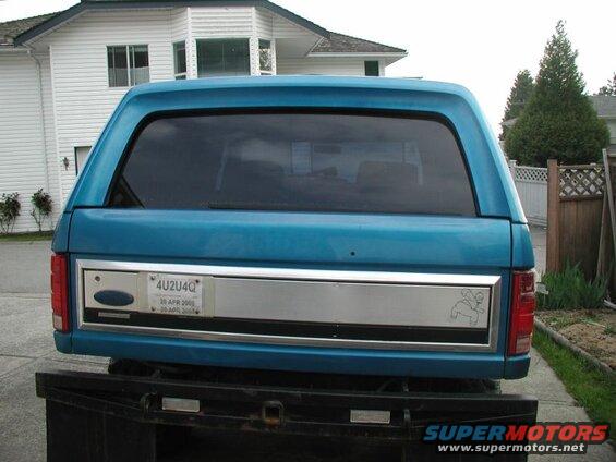 Rear view of a blue Ford Bronco with a camper shell, showing license plate and horse graphic.