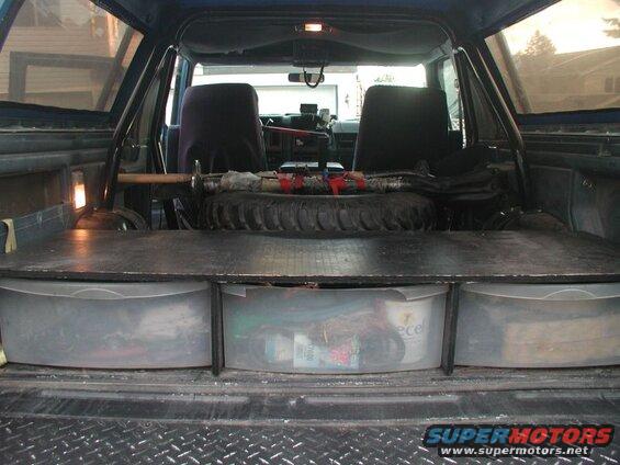 Interior rear of a blue Ford Bronco with custom storage bins and a spare tire.