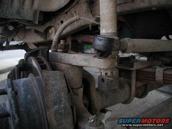 Close-up of rusty Ford Bronco front suspension components, tie rod end, knuckle, brake rotor.
