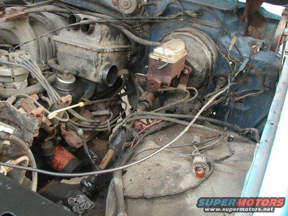 Engine bay of a blue 1985 Ford Bronco, showing brake booster, master cylinder, air intake, and wiring.
