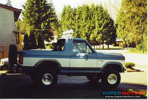 Lifted 1985 Ford Bronco, two-tone blue and white, side view, spare tire on rear.