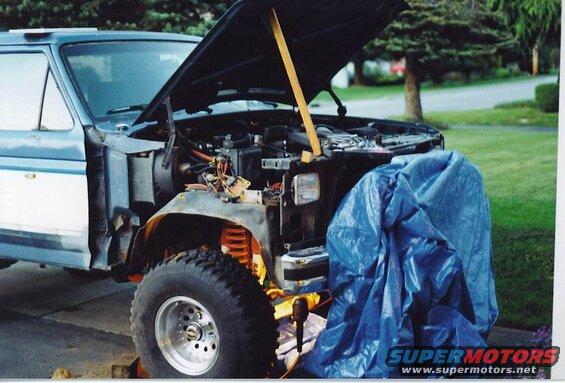 1985 Ford Bronco with hood open, engine exposed, front fender removed, blue tarp covering engine.