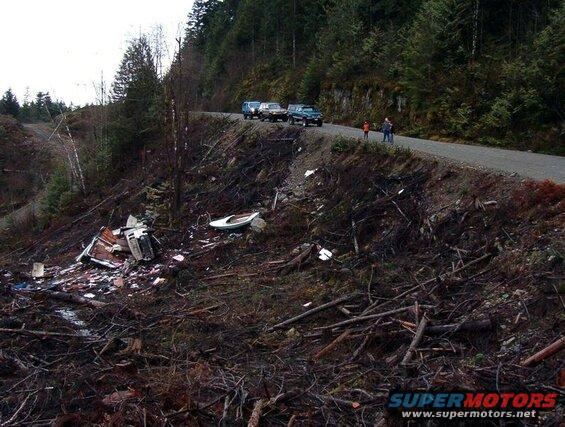 Debris and a small boat on a hillside next to a road with parked vehicles.