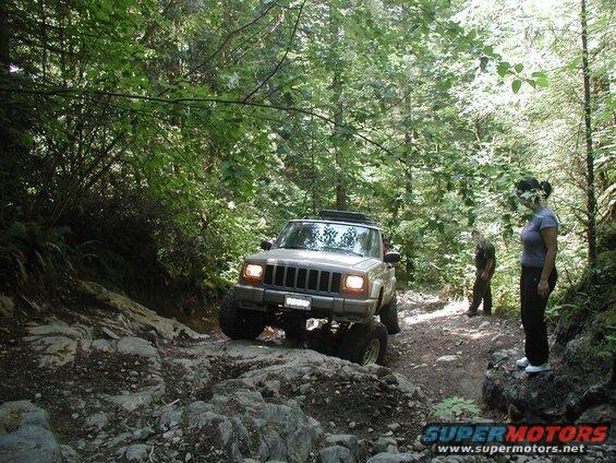 Tan Jeep Cherokee off-roading on a rocky, wooded trail.