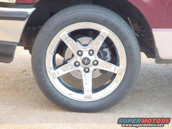 Chrome 5-spoke wheel with tire on a vehicle, showing brake caliper and rotor