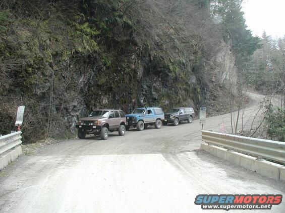 Three off-road vehicles parked on a gravel road next to a rocky embankment.