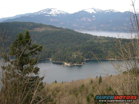Scenic view of a bay with forested hills and snow-capped mountains in the background.