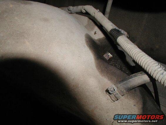 Underside of a vehicle showing a fuel tank with an oil leak and a damaged conduit.