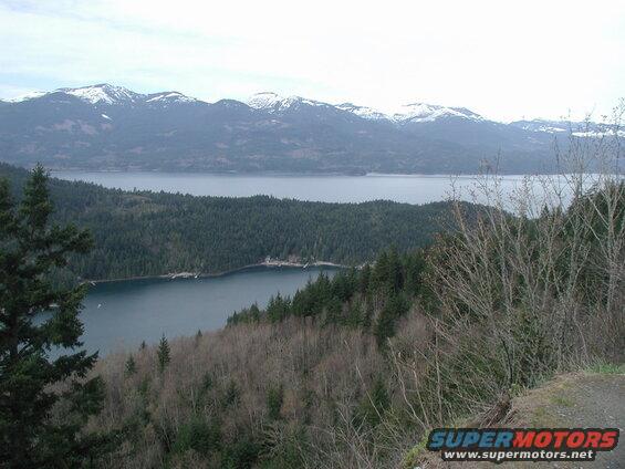 Scenic view of a lake or bay with forested hills and snow-capped mountains.
