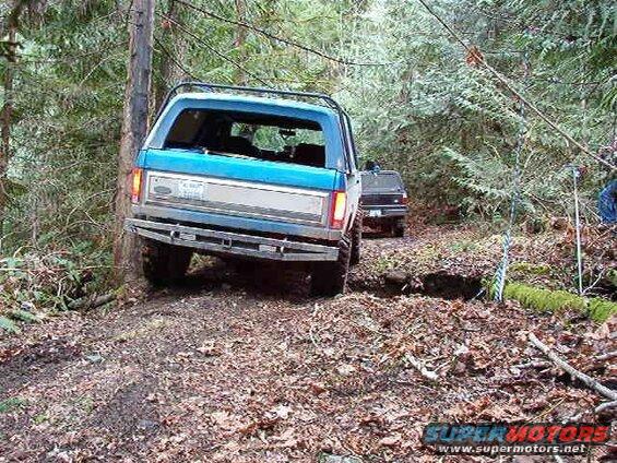 Blue Ford Bronco on a muddy forest trail, angled towards a ditch.