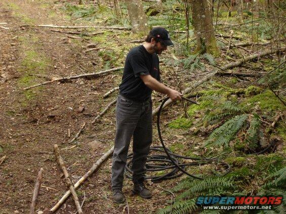 Man in a wooded area holding a black hose.