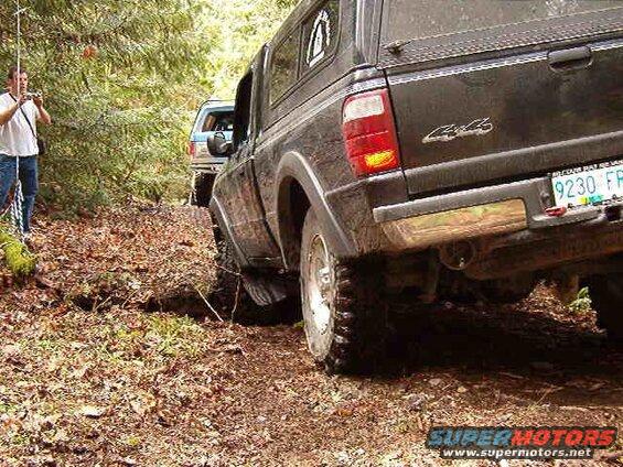 Off-road pickup truck driving on a dirt path with a camper shell.