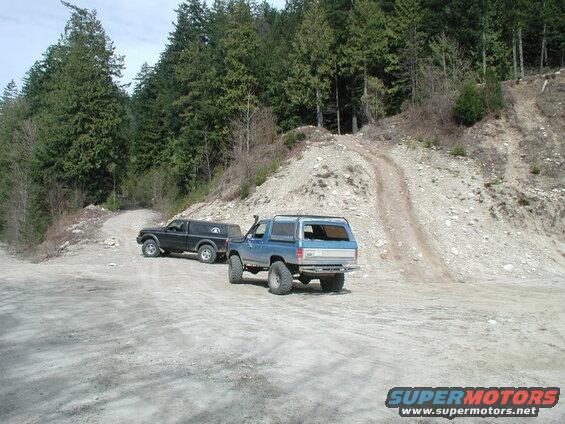 Two off-road vehicles on a dirt road in a forest.