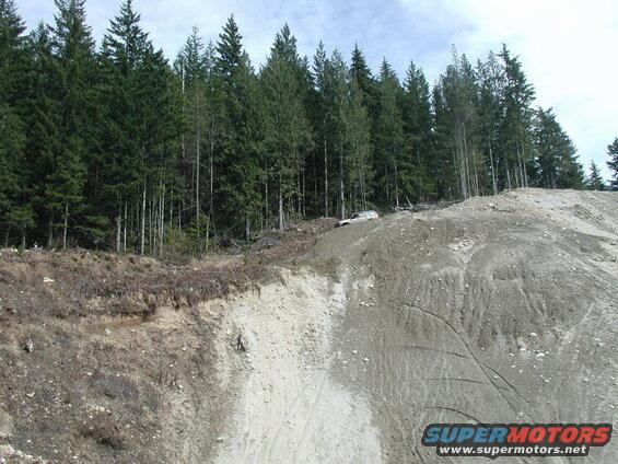 Light-colored SUV on a steep dirt slope with forest behind.