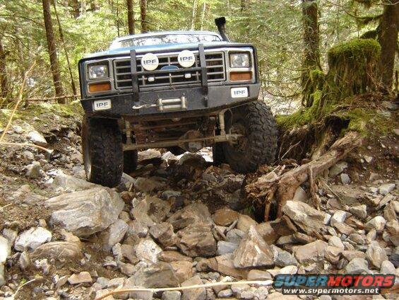 Blue Ford Bronco off-roading on a rocky trail in a forest.