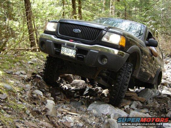 Black Ford pickup truck off-roading on a rocky trail in a forest.