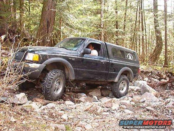 Black Ford pickup truck with camper shell on a rocky, wooded trail.
