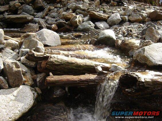 A stream flows over rocks and logs.