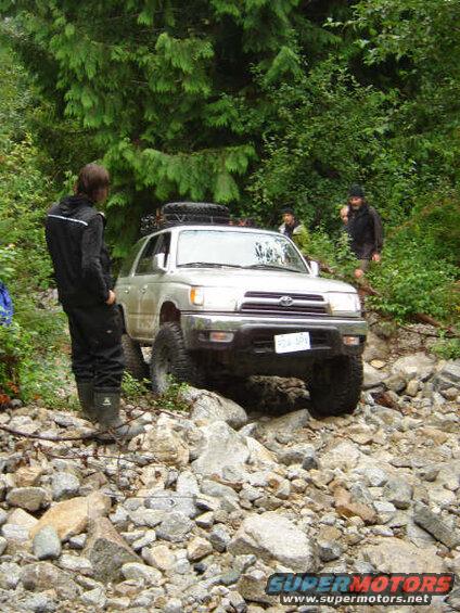 Silver SUV on a rocky trail with people.