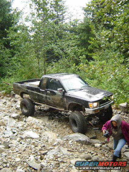Black Toyota pickup truck on a rocky off-road trail with a person walking behind.
