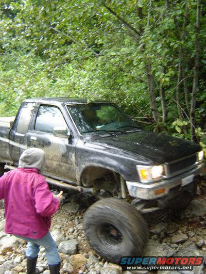 Black Toyota pickup truck on a rocky trail with a person in a pink jacket.