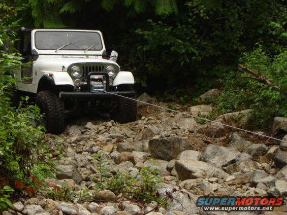 White Jeep CJ on a rocky trail with a winch and tow rope.