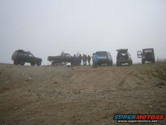 Several off-road vehicles and people on a dirt road in foggy conditions.