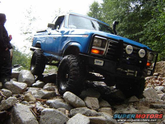 Lifted blue Ford Bronco driving over rocks on an off-road trail.