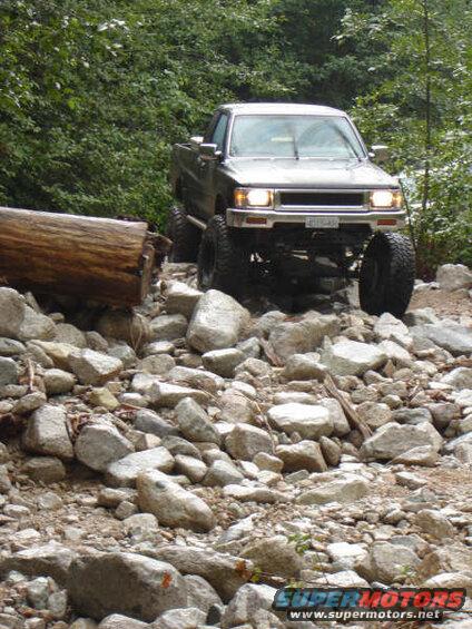 Lifted silver pickup truck driving over rocks on an off-road trail.